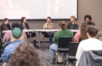 Five speakers sitting at a table, framed by audience